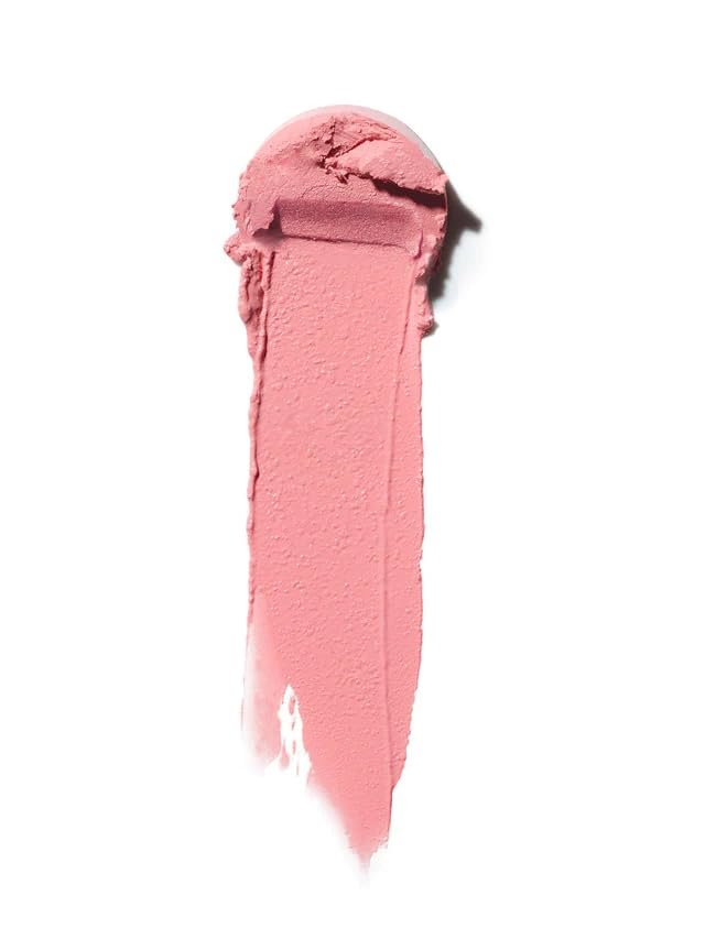 An ILIA Multi-Stick in the shade "Tenderly" swatched on a forearm, showing a soft, creamy pink color, with the stick itself resting nearby on a natural linen surface.