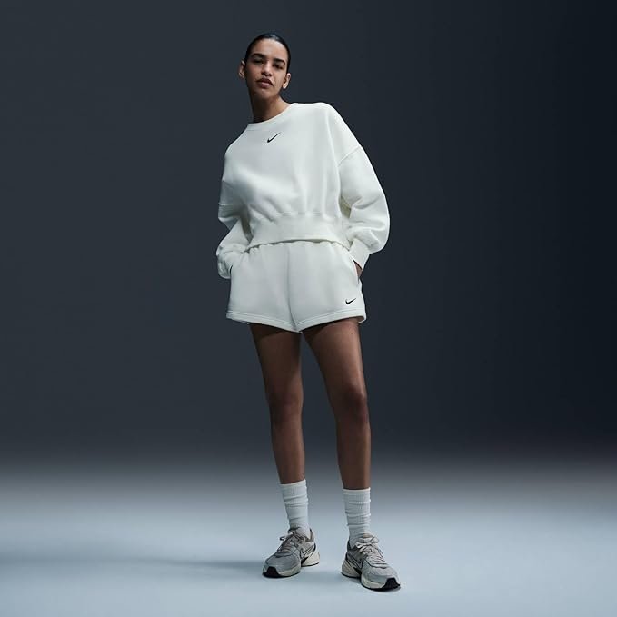 A woman wearing the Nike Sportswear Phoenix Fleece oversized crewneck in Sail/Black, paired with leggings, standing in a relaxed pose that highlights the dropped shoulder seams and relaxed fit.