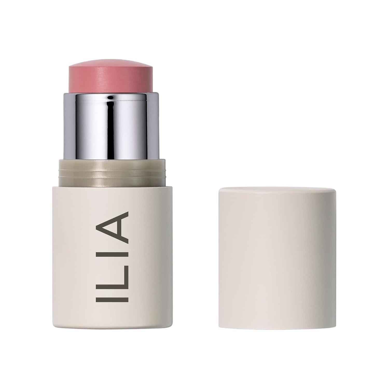 An ILIA Multi-Stick in the shade "Tenderly" swatched on a forearm, showing a soft, creamy pink color, with the stick itself resting nearby on a natural linen surface.