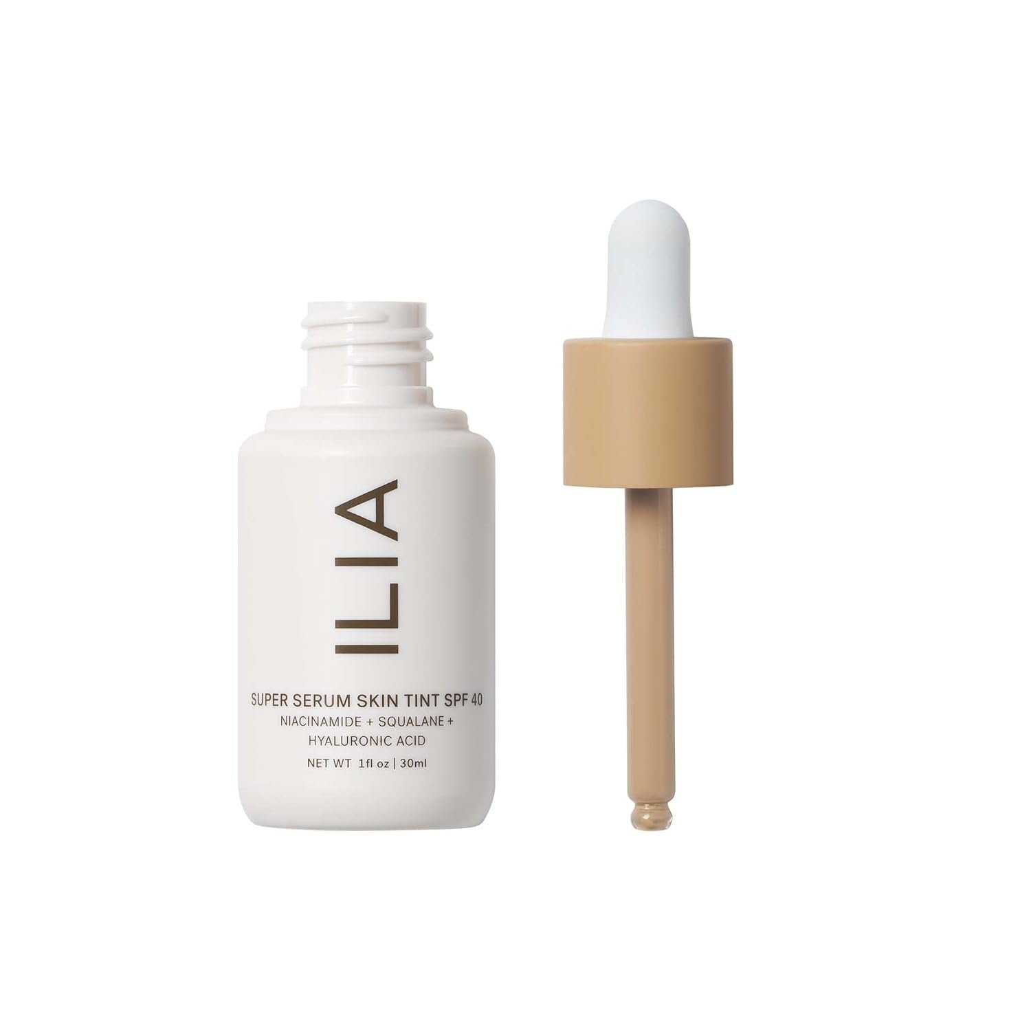 A bottle of ILIA Super Serum Skin Tint SPF 40 in the shade "Bom Bom" lying on its side next to a few pumps of the liquid tint on a white surface, highlighting its lightweight texture.