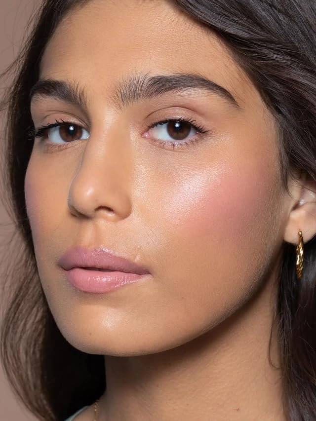 An ILIA Multi-Stick in the shade "Tenderly" swatched on a forearm, showing a soft, creamy pink color, with the stick itself resting nearby on a natural linen surface.