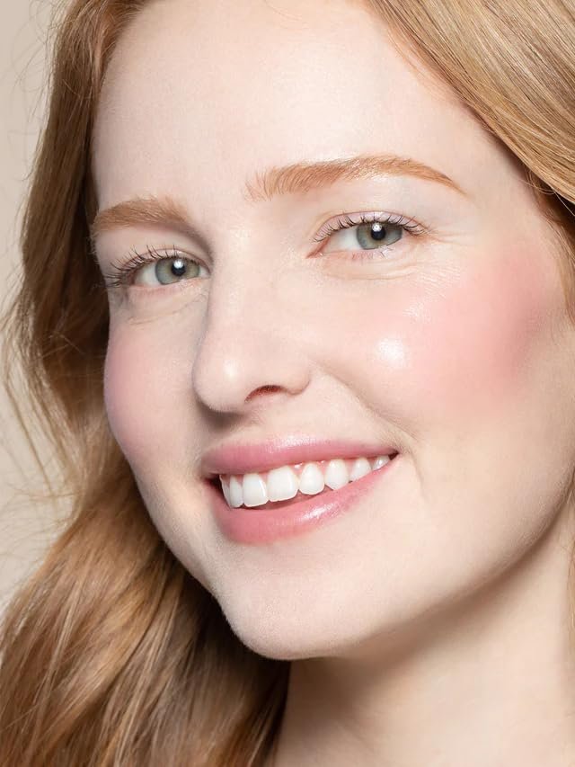 An ILIA Multi-Stick in the shade "Tenderly" swatched on a forearm, showing a soft, creamy pink color, with the stick itself resting nearby on a natural linen surface.