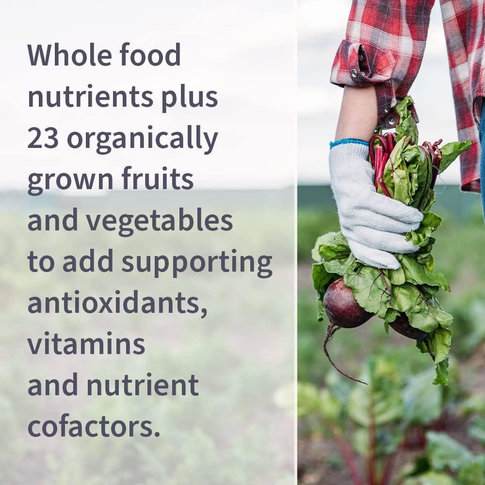 A bottle of Garden of Life Vitamin Code Women multivitamin capsules placed next to fresh organic fruits and vegetables like spinach, berries, and apples on a wooden surface.