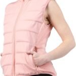 A woman wearing a dusty rose, quilted, weighted vest over a casual outfit is walking outdoors on a path surrounded by greenery, smiling and looking energized.