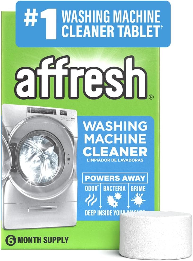 A hand holding an Affresh washing machine cleaner tablet above an open front-loading washer drum, with a clean, bright laundry room in the background.