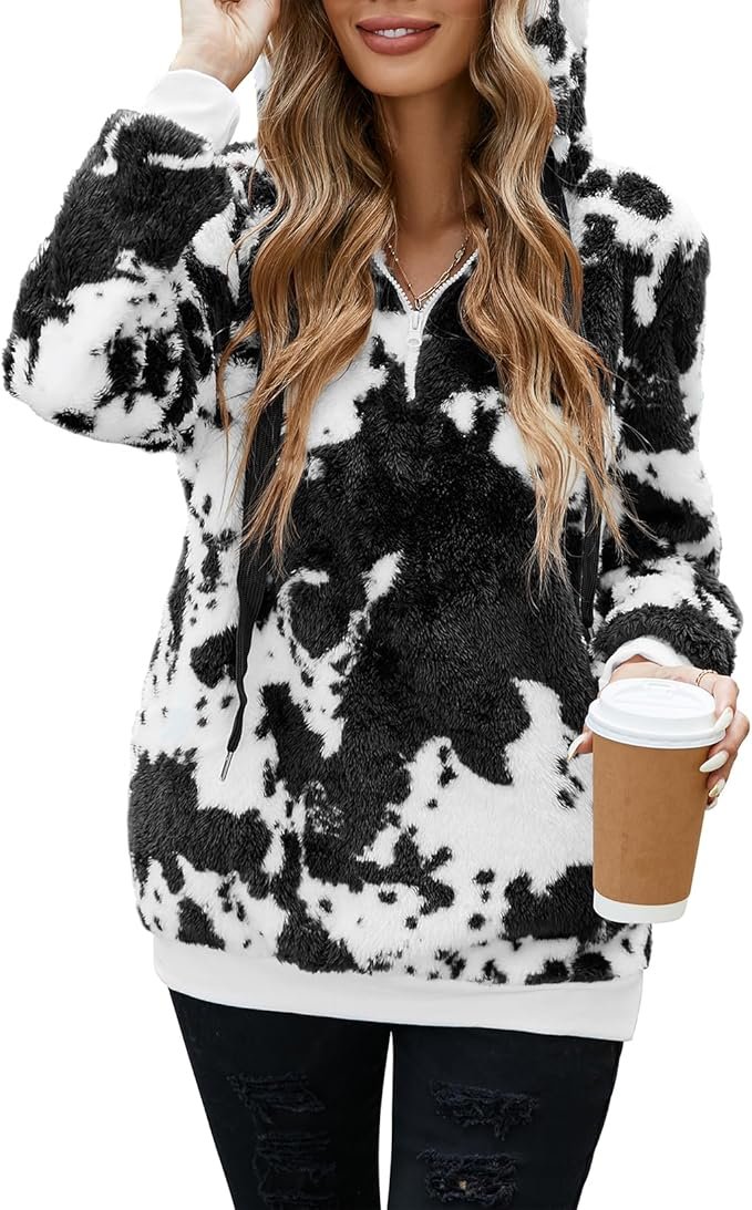 A woman wearing a soft, oversized gray fuzzy hoodie with a quarter-zip closure, sitting comfortably on a couch with a warm drink, embodying relaxation and comfort.