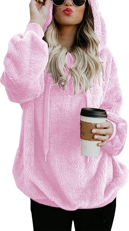 A woman wearing a soft, oversized gray fuzzy hoodie with a quarter-zip closure, sitting comfortably on a couch with a warm drink, embodying relaxation and comfort.