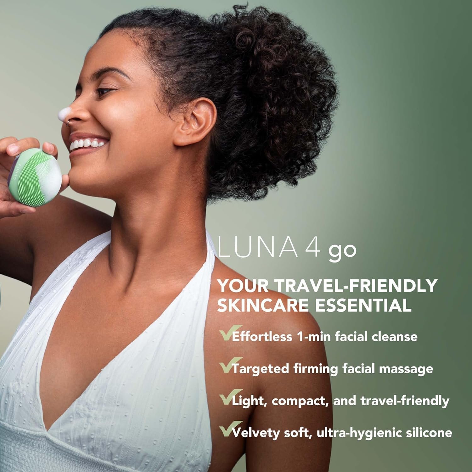 A close-up of the teal FOREO LUNA 4 Go facial cleansing and massaging device, held in a woman's hand against a soft, natural background with plants.