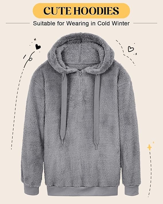 A woman wearing a soft, oversized gray fuzzy hoodie with a quarter-zip closure, sitting comfortably on a couch with a warm drink, embodying relaxation and comfort.