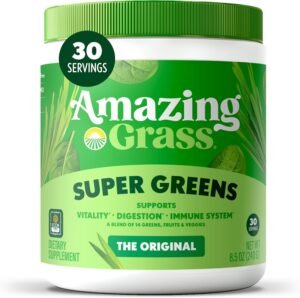A glass of vibrant green Amazing Grass Green Superfood drink is next to the green bag, with fresh spinach, kale, and an apple in the background, emphasizing the natural ingredients.