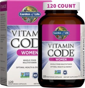A bottle of Garden of Life Vitamin Code Women multivitamin capsules placed next to fresh organic fruits and vegetables like spinach, berries, and apples on a wooden surface.