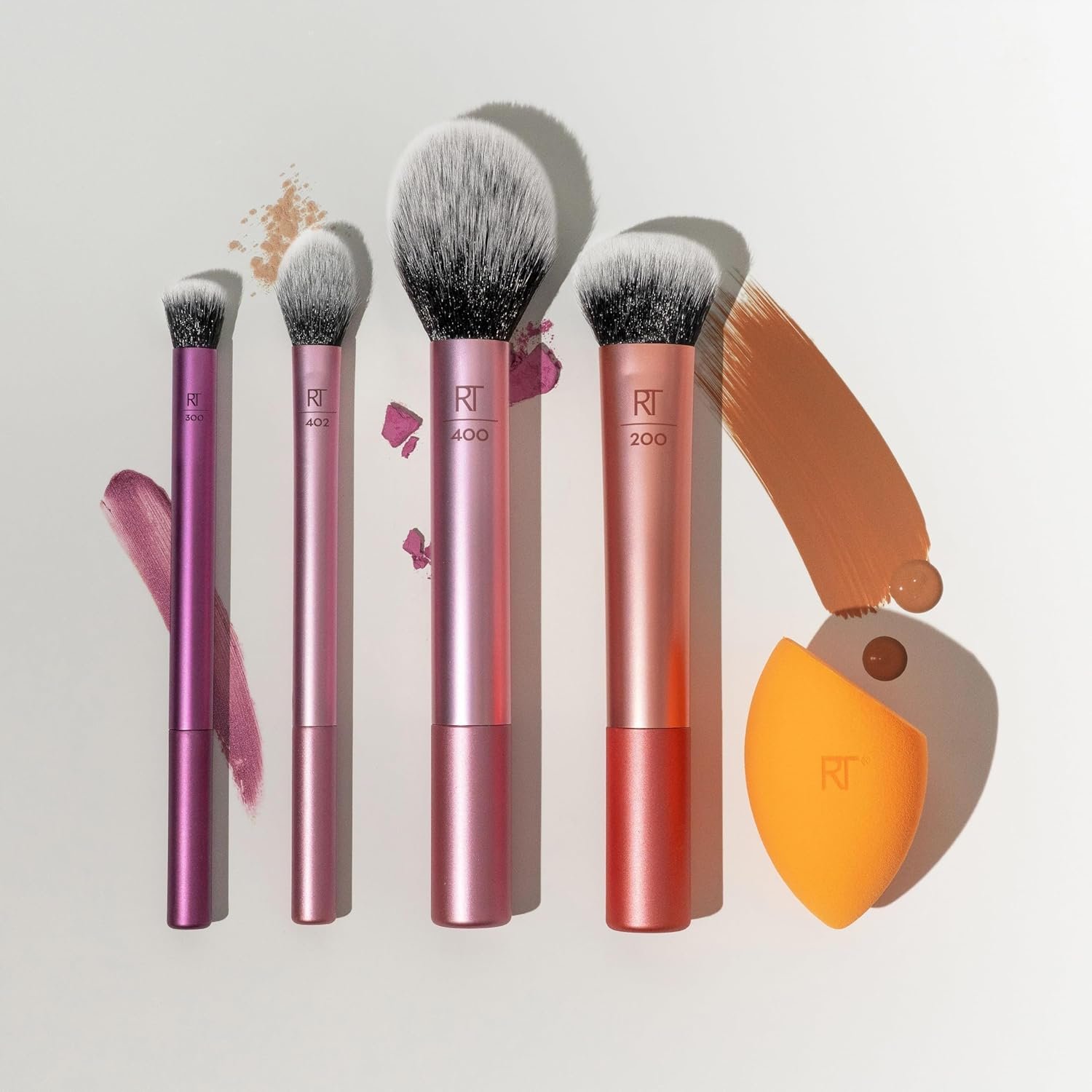 The Real Techniques A 5-piece Everyday Essentials makeup brush set laid flat, featuring four makeup brushes and one orange Miracle Complexion Sponge on a clean white background.